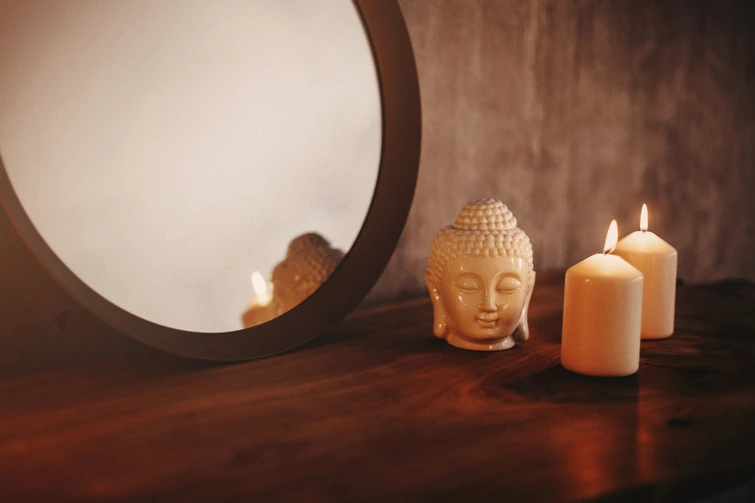 Peaceful Feng Shui Mirror Display with Candles A round mirror placed on a wooden shelf accompanied by burning candles and a small Buddha head statue.