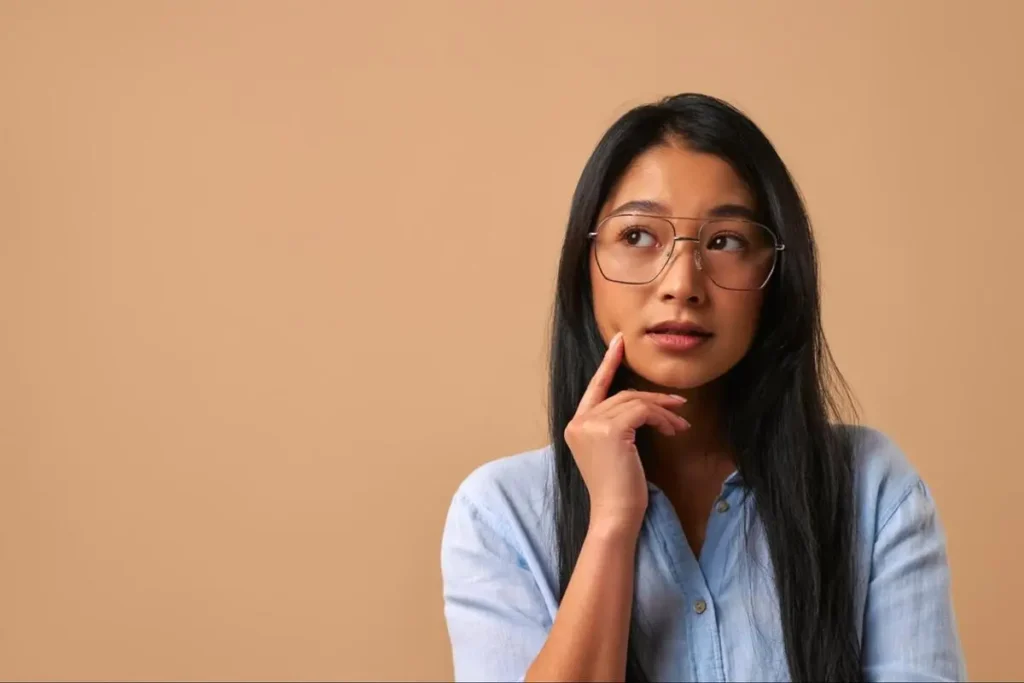 Young Asian woman with glasses looking upward thoughtfully representing someone seeking clarity through a Bazi consultation in Singapore