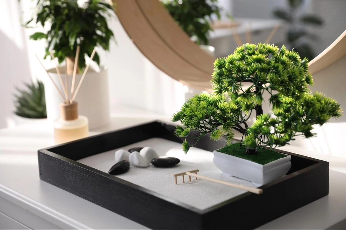 Small zen garden with bonsai tree, white and black stones arranged on a dark wooden tray