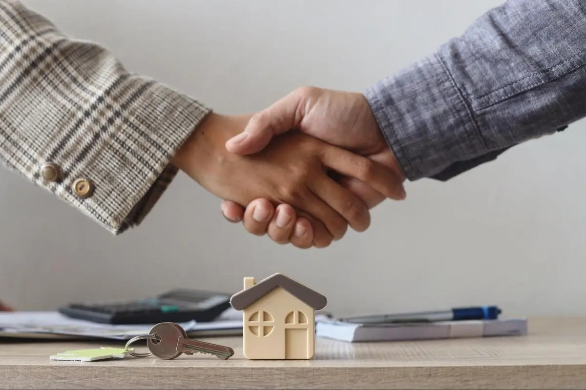 Two people shaking hands beside a model house and keys